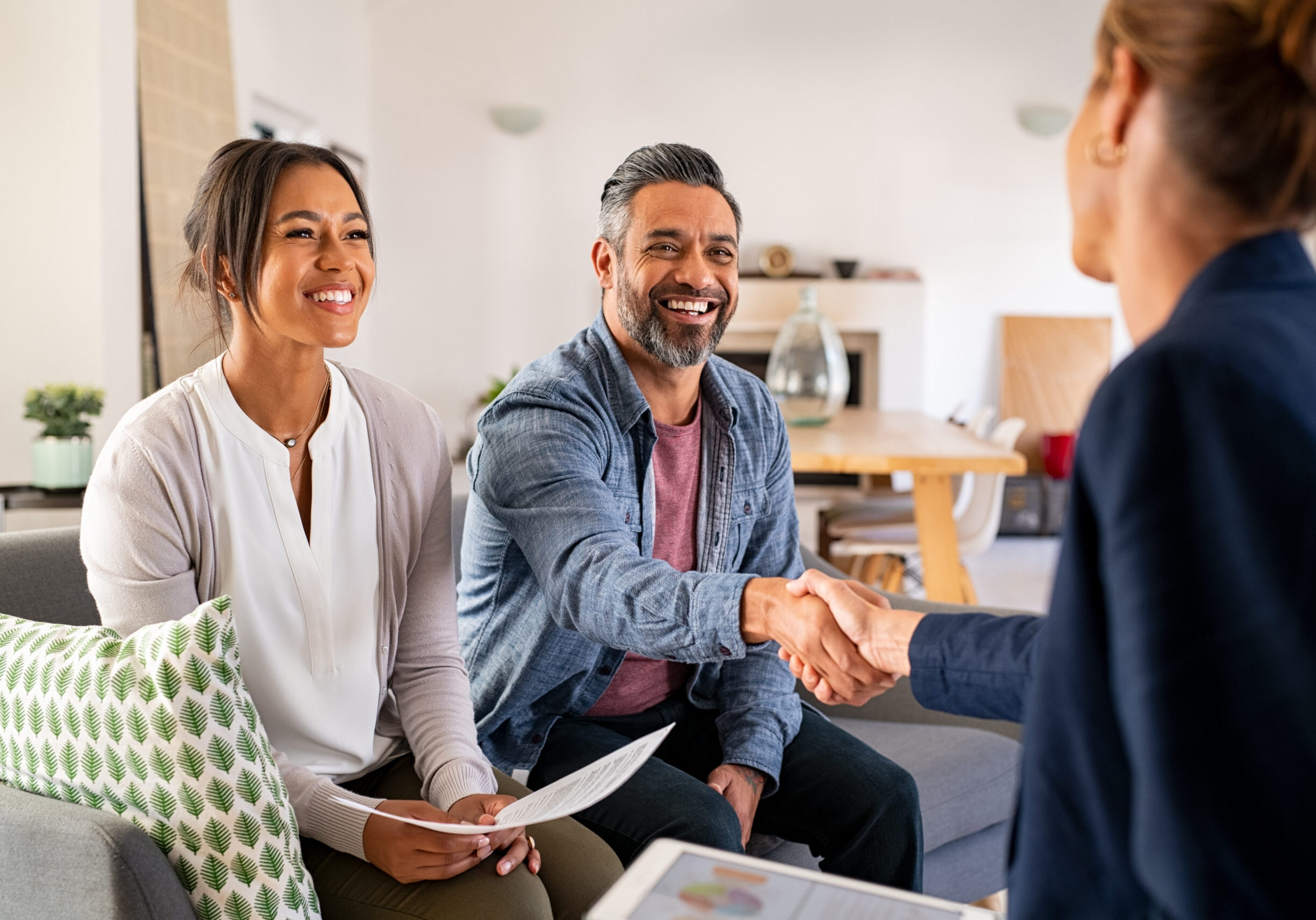 Multiethnic couple handshake with consultant at home Mature indian man shaking hands with financial advisor at home. Happy smiling couple greeting broker with handshake at home. Multiethnic mid adult man and hispanic woman sealing a contract.